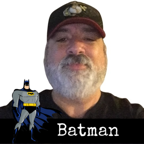A man with a gray beard wearing a cap is pictured with a cartoon Batman figure and the word "Batman" at the bottom.