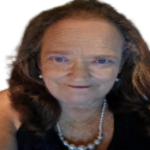A woman with long brown hair, wearing a black top and a pearl necklace, smiles at the camera against a plain background.